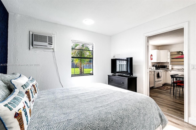 bedroom featuring a textured wall, wood finished floors, and a wall mounted AC