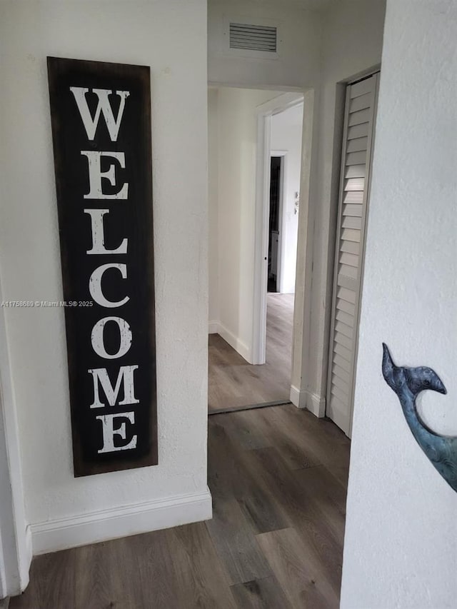 hallway featuring visible vents, baseboards, and wood finished floors