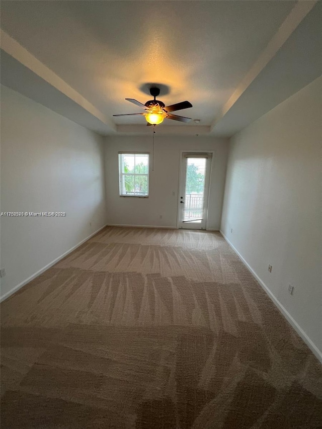 unfurnished room with ceiling fan, a tray ceiling, light colored carpet, and baseboards