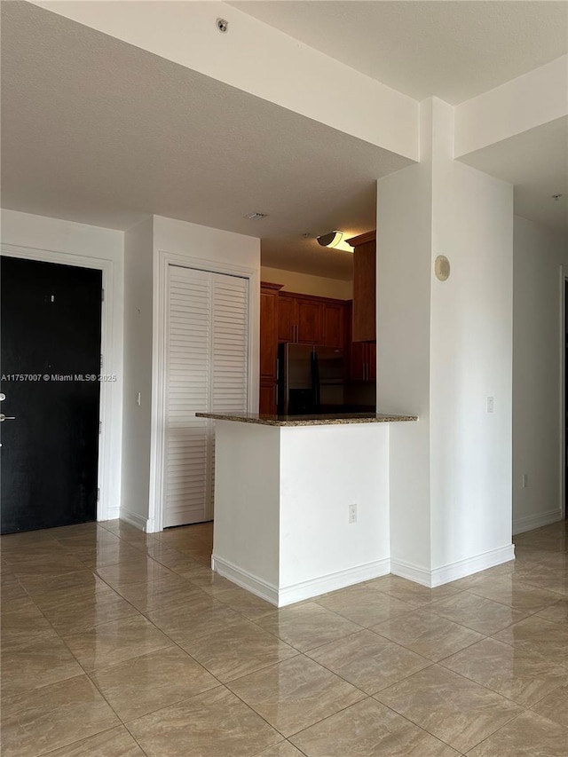 kitchen with refrigerator, dark stone counters, a peninsula, and baseboards