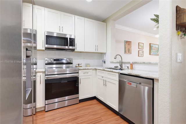 kitchen with light wood finished floors, ornamental molding, a sink, stainless steel appliances, and backsplash