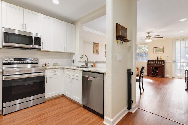 kitchen with light wood-style flooring, stainless steel appliances, a sink, white cabinets, and backsplash