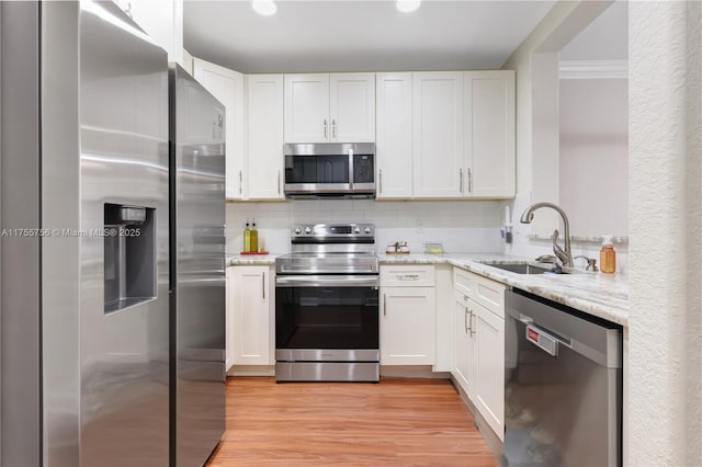 kitchen with stainless steel appliances, tasteful backsplash, light wood-style floors, a sink, and light stone countertops