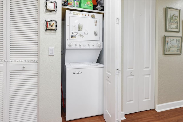 laundry area featuring a textured wall, laundry area, wood finished floors, baseboards, and stacked washer / drying machine