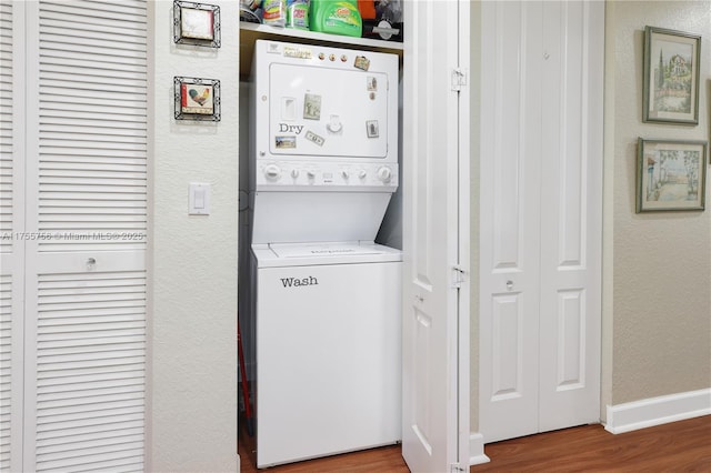 clothes washing area with laundry area, wood finished floors, stacked washing maching and dryer, a textured wall, and baseboards