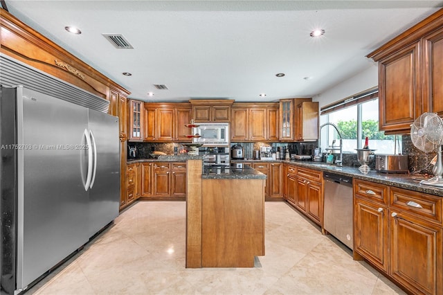 kitchen featuring visible vents, brown cabinetry, a kitchen island, a sink, and built in appliances