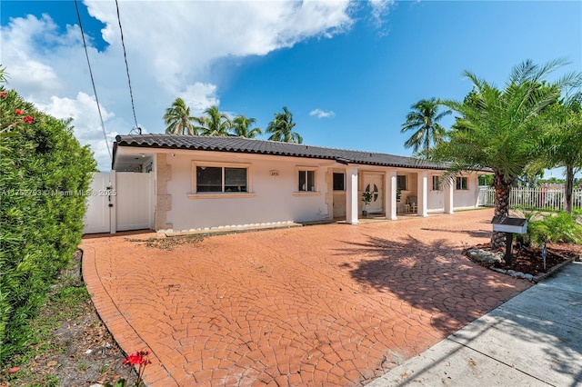 rear view of property with a gate, fence, a tiled roof, and stucco siding