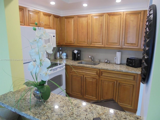 kitchen with recessed lighting, brown cabinetry, a sink, light stone countertops, and white appliances