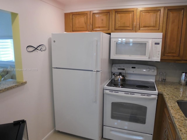 kitchen with white appliances, light stone counters, and brown cabinets