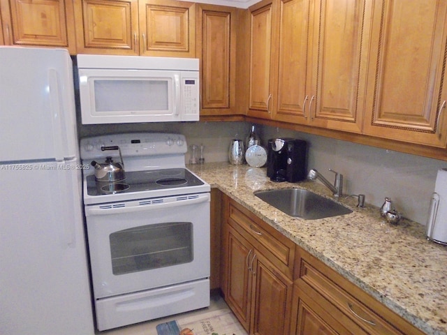 kitchen with brown cabinetry, white appliances, a sink, and light stone counters