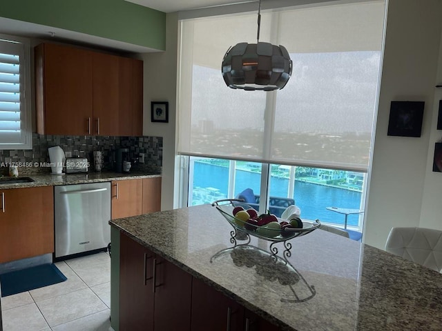 kitchen featuring tasteful backsplash, dishwasher, dark stone countertops, a sink, and light tile patterned flooring