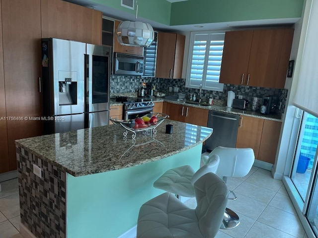 kitchen featuring light tile patterned floors, decorative backsplash, appliances with stainless steel finishes, a center island, and a sink