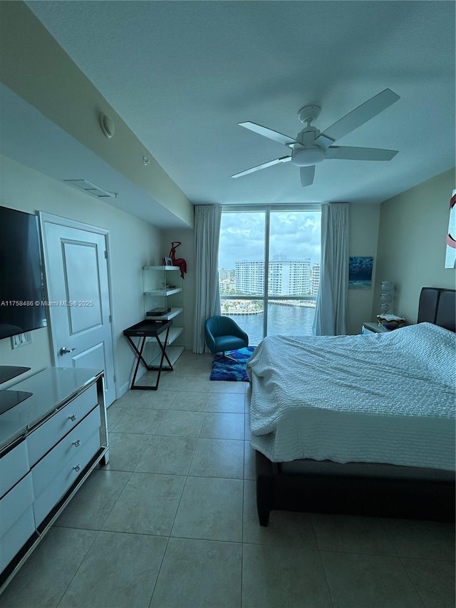 bedroom featuring ceiling fan, tile patterned flooring, visible vents, and a wall of windows