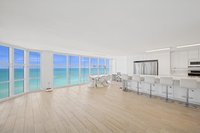 interior space featuring light wood-type flooring, a water view, and floor to ceiling windows