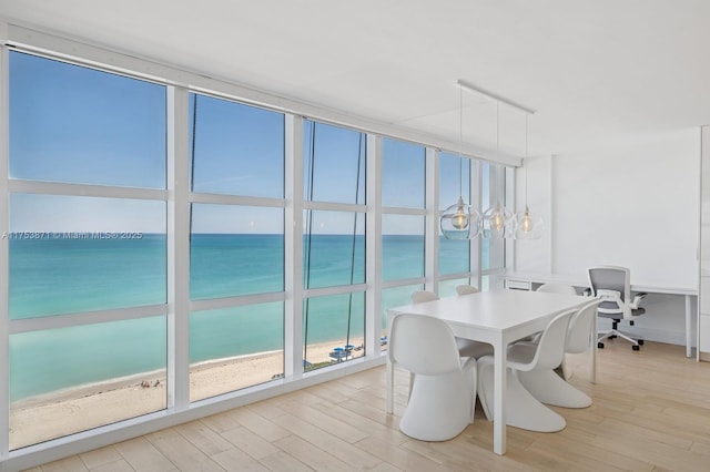 dining area with a water view, light wood-style flooring, a beach view, and a wall of windows