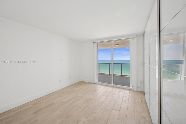 empty room featuring a water view, light wood-style flooring, baseboards, and a wall of windows