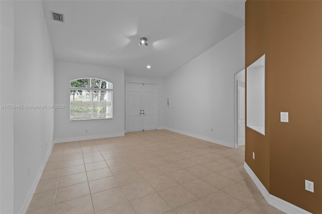 empty room featuring light tile patterned floors, visible vents, baseboards, and vaulted ceiling