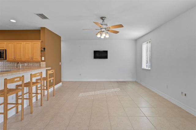 living area with light tile patterned floors, a ceiling fan, visible vents, and baseboards