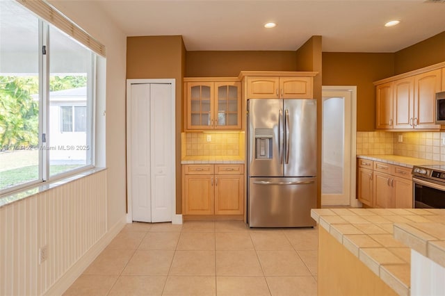 kitchen with tile countertops, plenty of natural light, glass insert cabinets, and stainless steel appliances