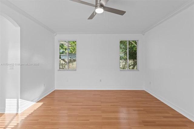 spare room featuring light wood finished floors, arched walkways, baseboards, and ornamental molding