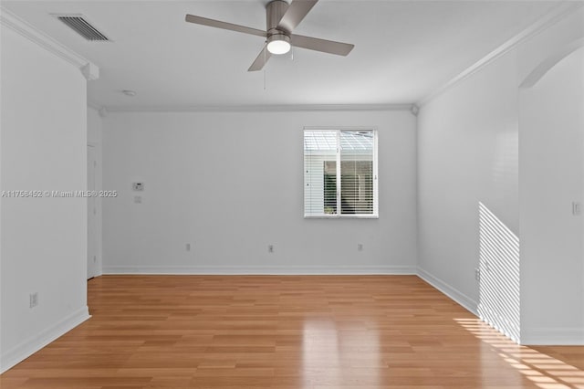 empty room with arched walkways, visible vents, light wood finished floors, and ornamental molding