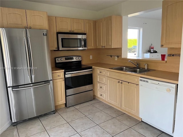 kitchen with appliances with stainless steel finishes, light countertops, light brown cabinets, a sink, and light tile patterned flooring