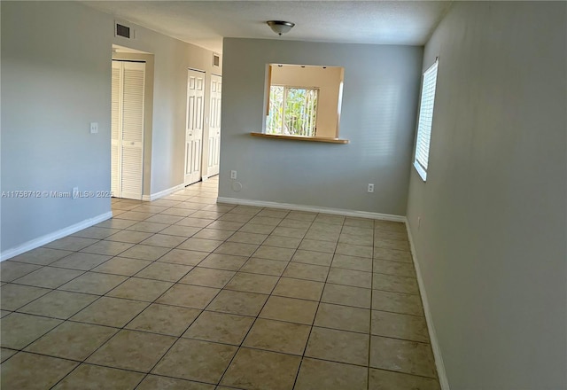 tiled spare room featuring a healthy amount of sunlight, visible vents, a textured ceiling, and baseboards