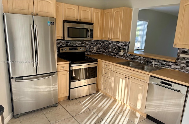 kitchen with decorative backsplash, stainless steel appliances, a sink, and light brown cabinetry