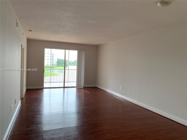 unfurnished room featuring visible vents, dark wood finished floors, a textured ceiling, and baseboards