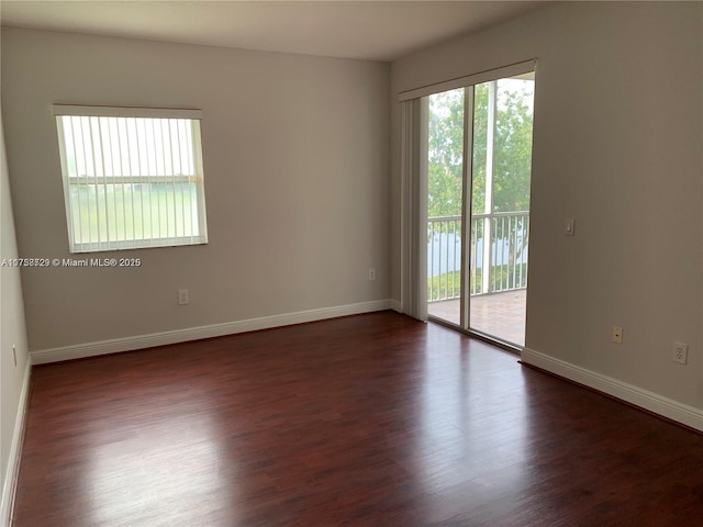 unfurnished room with baseboards, dark wood-style flooring, and a wealth of natural light