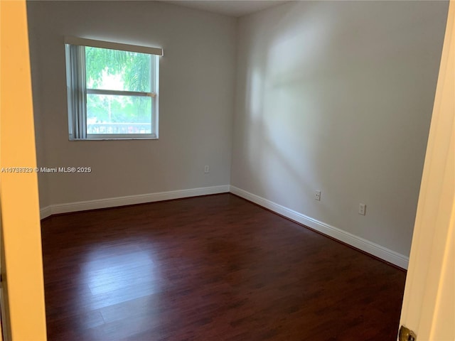 spare room featuring dark wood-type flooring and baseboards