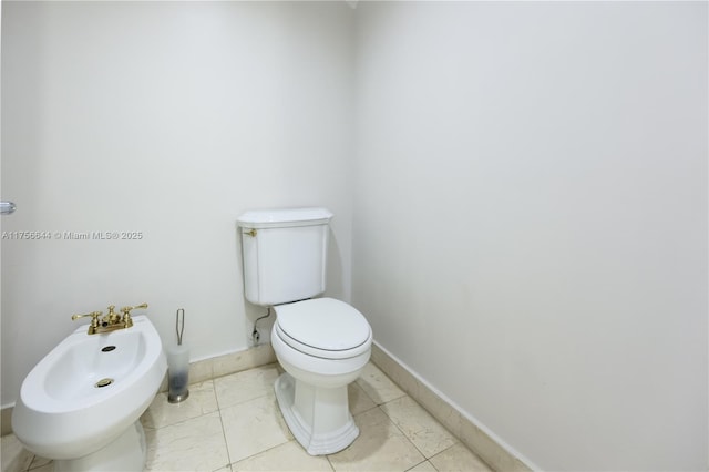 bathroom featuring tile patterned flooring, toilet, a bidet, and baseboards