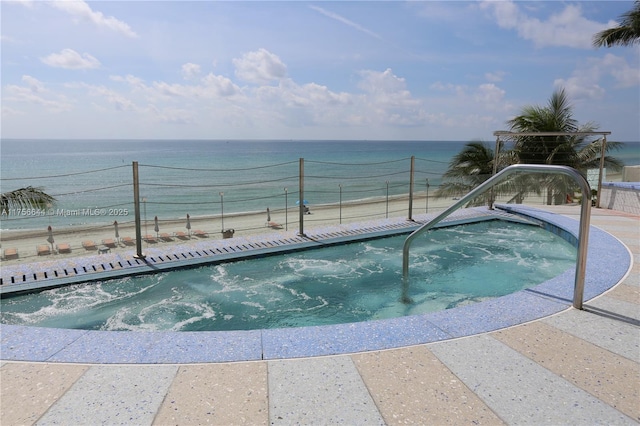 view of swimming pool featuring an in ground hot tub, a water view, a view of the beach, and fence