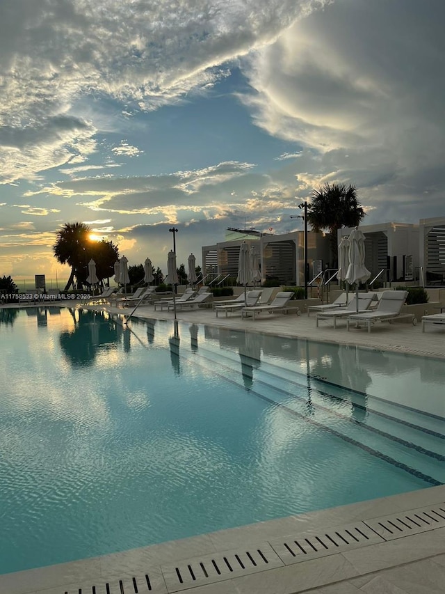 pool at dusk featuring a patio area and a community pool