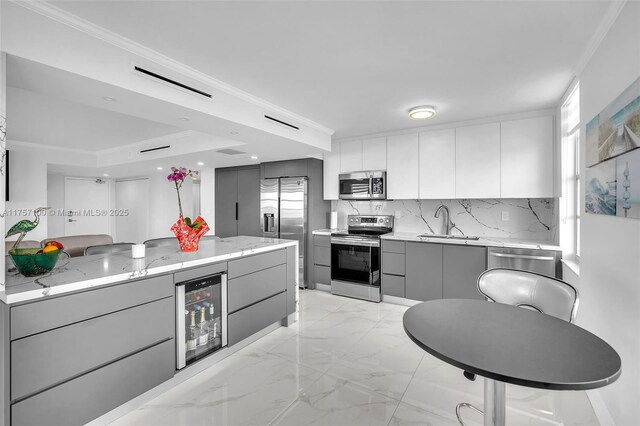 kitchen featuring wine cooler, appliances with stainless steel finishes, ornamental molding, gray cabinetry, and a sink