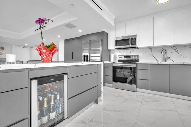 kitchen featuring beverage cooler, appliances with stainless steel finishes, a raised ceiling, and gray cabinetry