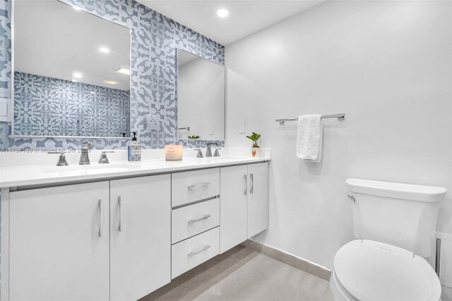 full bath featuring double vanity, a sink, toilet, and wallpapered walls