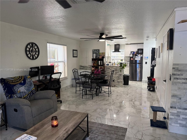 living room with a ceiling fan, marble finish floor, and a textured ceiling