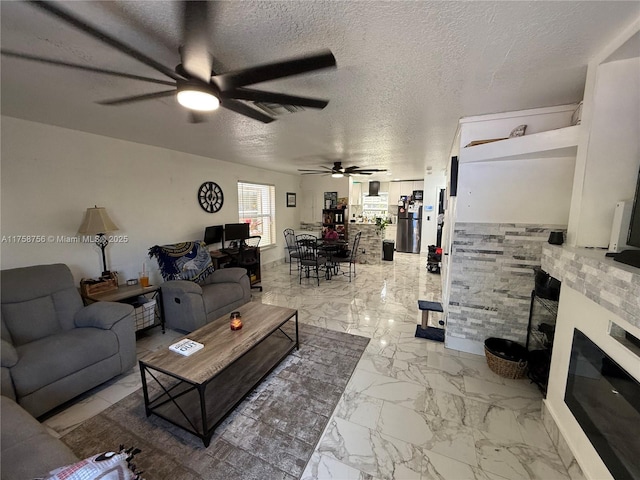living area featuring a ceiling fan, marble finish floor, a fireplace, and a textured ceiling