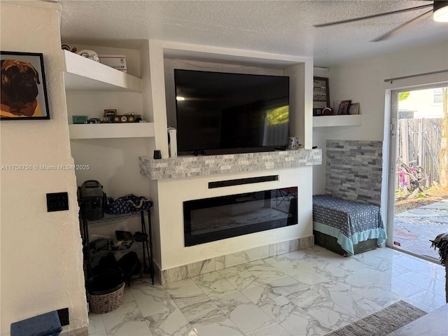 living room featuring a ceiling fan, a glass covered fireplace, marble finish floor, and a textured ceiling