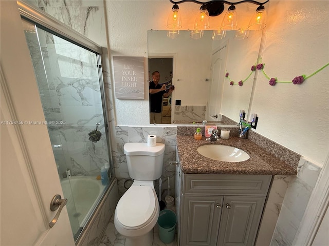 bathroom featuring a textured wall, toilet, shower / bath combination with glass door, marble finish floor, and vanity