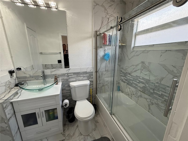 bathroom with marble finish floor, tile walls, toilet, combined bath / shower with glass door, and vanity