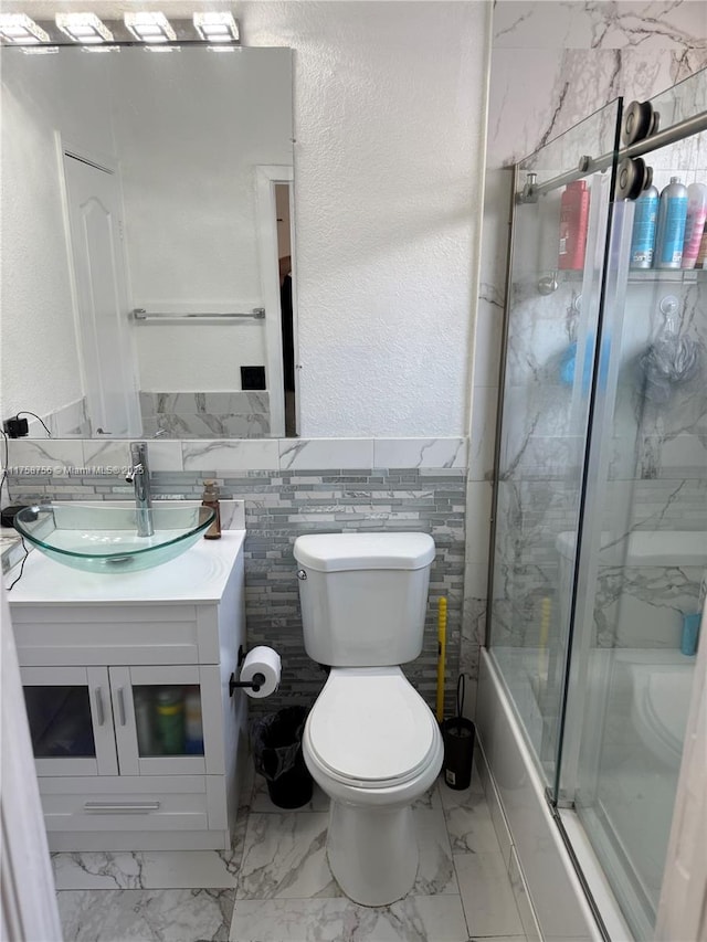 bathroom with a textured wall, toilet, marble finish floor, vanity, and tile walls