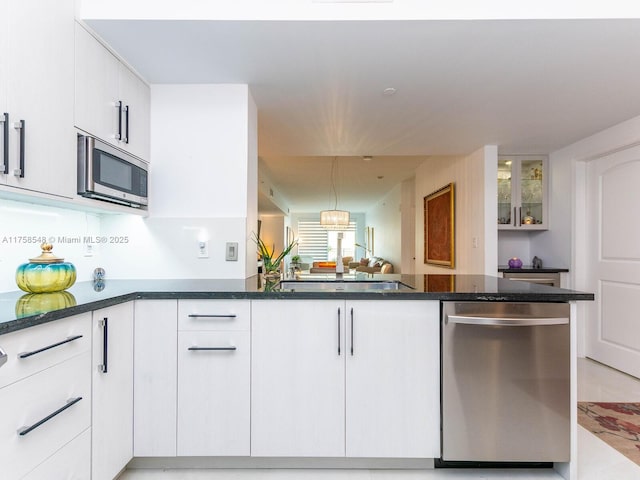 kitchen featuring appliances with stainless steel finishes, glass insert cabinets, white cabinetry, dark stone counters, and a peninsula