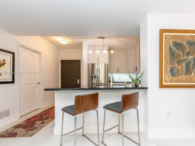 kitchen with a peninsula, visible vents, baseboards, a kitchen breakfast bar, and stainless steel fridge