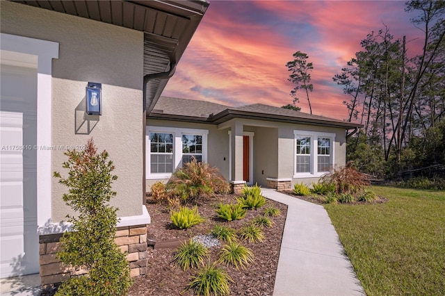 view of front of property featuring a garage, a shingled roof, a lawn, and stucco siding