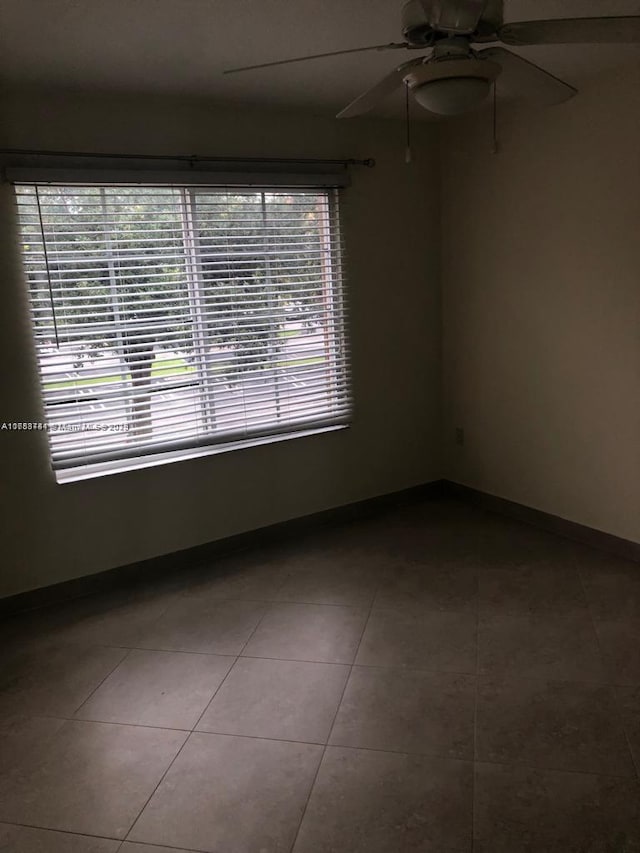 tiled empty room featuring ceiling fan and baseboards