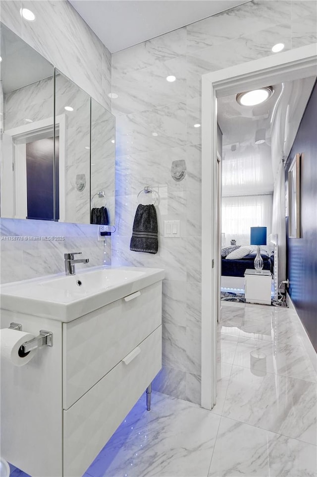 bathroom with marble finish floor, tile walls, and vanity