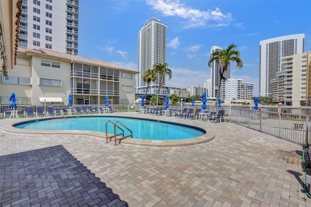 community pool featuring a view of city, a patio, and fence