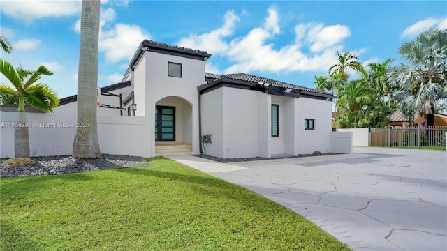 rear view of house with a lawn, a tiled roof, a gate, fence, and stucco siding